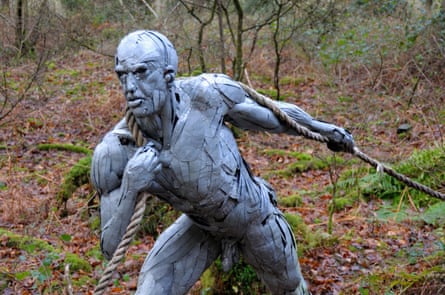 Sculpture of a naked man pulling ropes in a forest