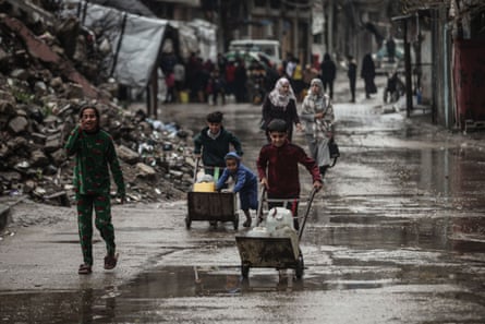Children wheel containers of water through the street in Nusairat.