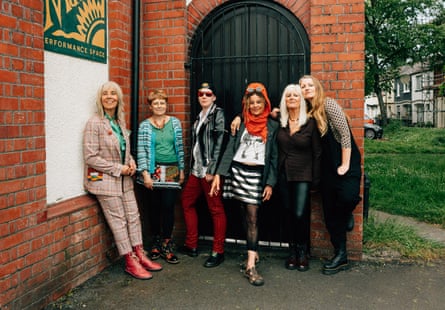 A punk group of women posing in front of a black door to a redbrick building
