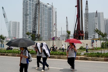 High school students use umbrellas and jackets to shield themselves from the heat while crossing a street near a construction site in Hanoi