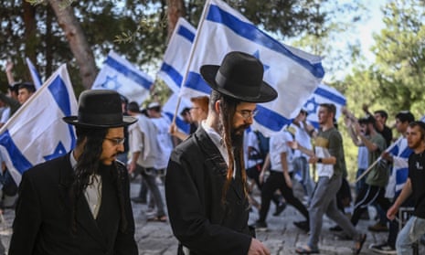 Two ultra-Orthodox men walk past religious Israeli pre-military aged youth, who wave their national flag as they protest outside the Old City of Jerusalem in support of Israel on Thursday.