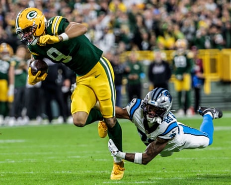 Packers receiver Christian Watson leaps forward while tackled by a Panthers defender