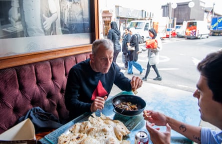Two men sitting at a banquette table with a bowl of curry and a naan bread on the table in front of them
