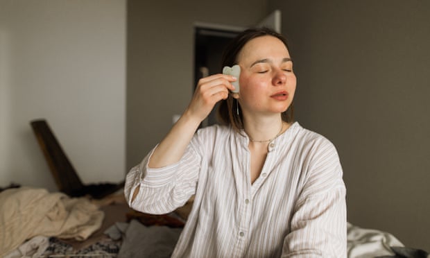 A portrait of a young woman doing gua sha massage facial at home