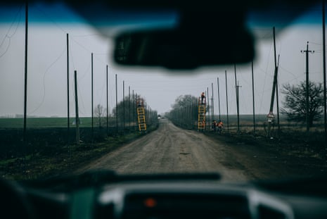 View from inside a car of workers using two ladders to construct netting on posts that line both sides of a road