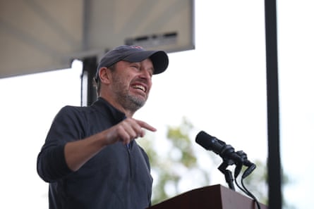 a man in a peaked cap speaks on stage