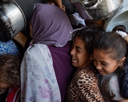 Children holding pans are squashed together as they attempt to get food from a charity kitchen.