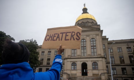 A woman holds a sign saying 'Cheaters' in front of the Georgia state capitol.