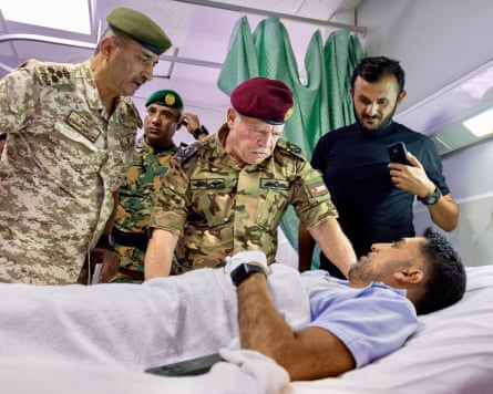 King Abdullah II of Jordan, with officers, visits a patient lying in a hospital bed