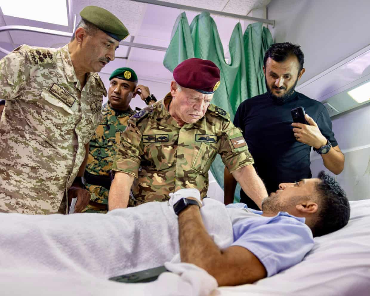 King Abdullah II of Jordan, with officers, visits a patient lying in a hospital bed