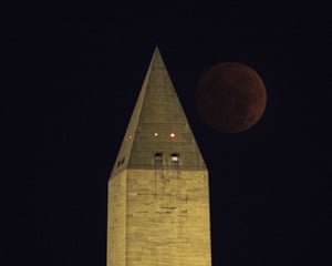 The reddish moon darkens in the sky next to the Washington Monument in Washington DC