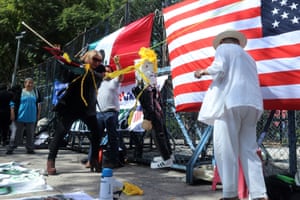 a woman hits a piñata outside, an American flag and a Mexican flag hung up in front of her
