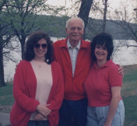Two sisters standing either side of their father, in front of a lake