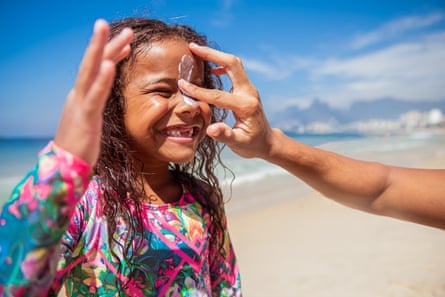 a child at the beach getting sunscreen applied to her face