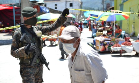 An elderly man is granted entry to the market by a masked armed soldier in Nebaj