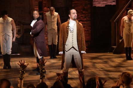 A man performs as Alexander Hamilton with a troupe of other actors of color wearing historical costumes