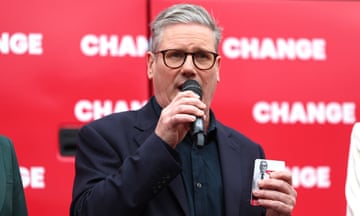 Keir Starmer holdng microphone in front of a red Labour banner with the word 'Change' on it