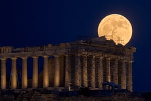The strawberry moon rises in the sky behind the 5th century BC Parthenon temple at the ancient Acropolis hill, Athens, Greece.