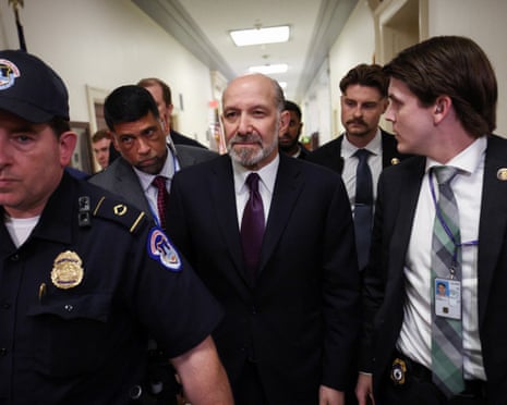Howard Lutnick, in a black suit and purple tie, arrives flanked by police and men in suits