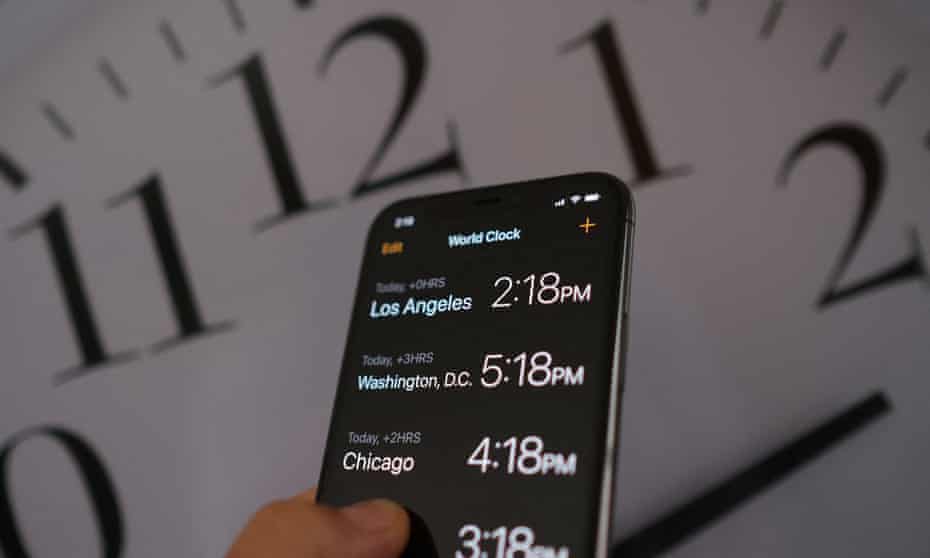 A clock in the background of a smartphone showing the time after daylight saving time was implemented in Los Angeles, California, on March 15, 2022.