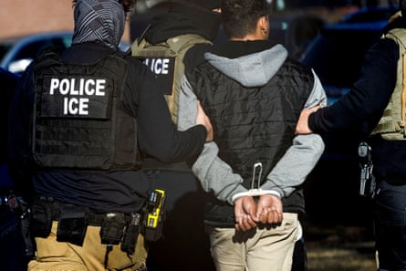 A man with his hands cuffed behind his back is led away by men wearing body armour which reads 'Police ICE'