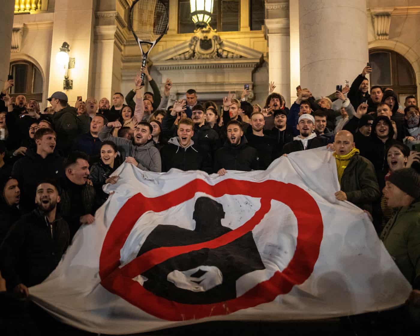 Celebrating election supporters in Belgrade hold a banner with a crossed-out silhouette at night