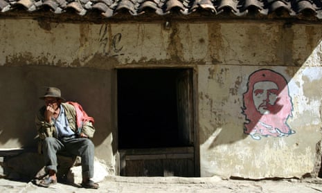 A man sits outside a house next to the image of Che Guevara in La Higuera, Bolivia.
