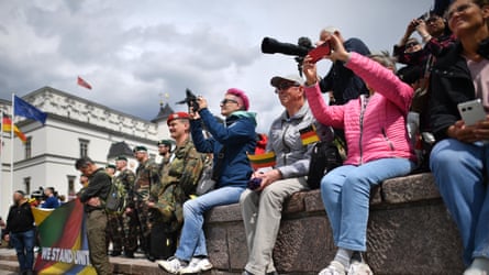 People with cameras and flags sitting on wall and troops in background