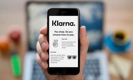 A man looks at his iPhone which displays the Klarna logo
