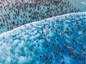 An aerial view of hundreds of people swimming or standing in bright blue water