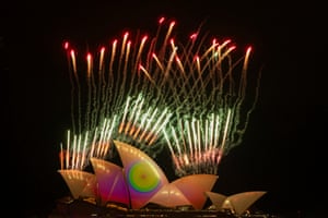 Fireworks emerge above the Sydney Opera House, which has colourful lights shining on to it