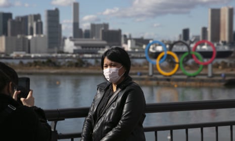 A tourist wearing a mask poses for a photo with the Olympic rings in the background, at Tokyo’s Odaiba district. 