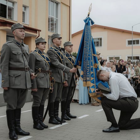 The senior student leader bows before a blue and gold flag and four personnel who wear formal grey uniform. He wears a white shirt and black trousers.