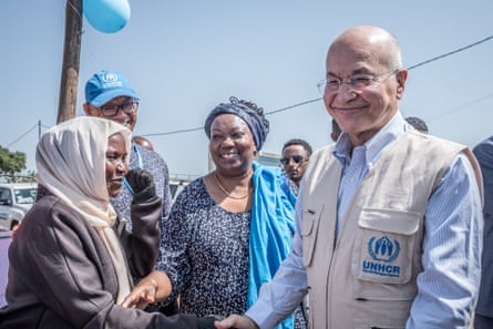 A smiling man shakes the hand of a woman as another woman and a man look on