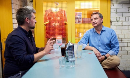 Two men, both wearing blue shirts, sitting at a restaurant table talking