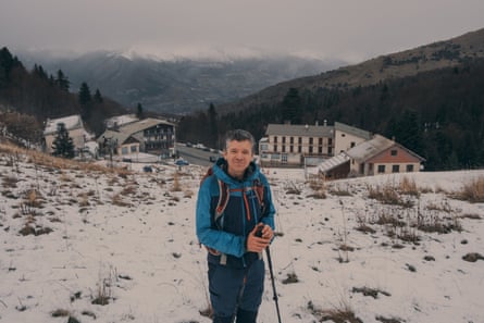 A man in a blue ski jacket stands on a snowy slope holding a ski pole.