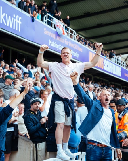 Millwall fans stands on railing and celebrates as another fan stands below him fist clenched in the air.