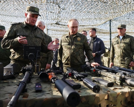 Vladimir Putin and several soldiers inspect a table of military weaponry