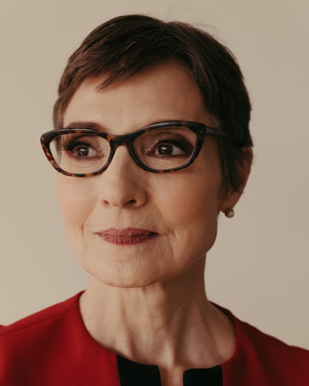 portrait of a woman with short hair, glasses, in a red dress against a beige wall