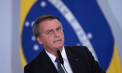 President Jair Bolsonaro should be charged with “crimes against humanity,” a panel of lawmakers said in October. He stands in front of a Brazil flag in a dark suit.