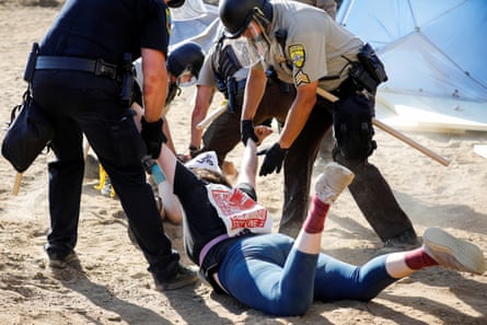 police officers stand over a person on the ground while restraining that person’s arms