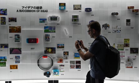 A visitor takes photos of a showcase display with Nintendo consoles in it.