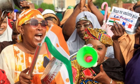 Women waving Niger flags, blowing horns and holding placards.