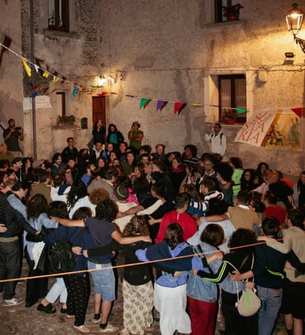 A crowd of people linking arms in a medieval street, with bunting and a Sustarìa banner above them
