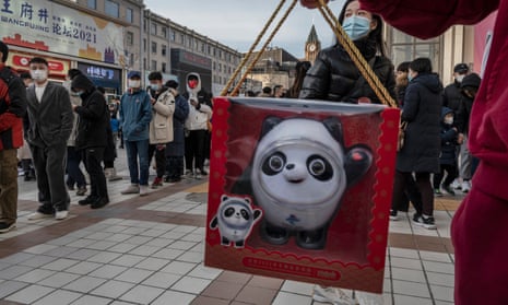 A man holds a toy of mascot Bing Dwen Dwen he just bought as people line up with hundreds of others to enter the official Beijing 2022 Winter Olympics store to buy merchandise.