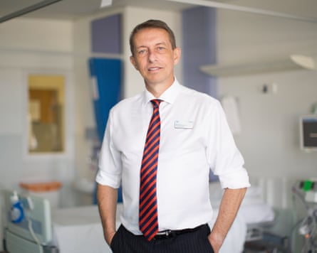 NHS leader Matthew Hopkins, wearing a white shirt and striped tie, stands in a hospital ward.