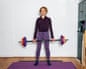 Standing on an exercise mat, she holds a weighted barbell at her waist