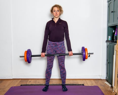 Standing on an exercise mat, she holds a weighted barbell at her waist
