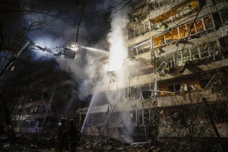 Firefighters spray water on to a smoke-filled, bomb-damaged apartment building in Kyiv at night