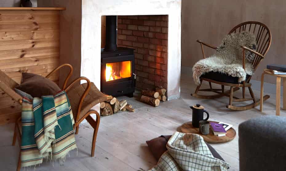 A rocking chair with a fleece on it and a reclined chair with a cushion and throw, either side of a fireplace with a lit log-burning stove